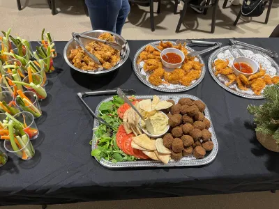 Buffet table with veggie cups, fried items, hummus, pita, and greens.