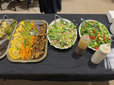 Buffet table with trays of grilled vegetables, Caesar salad, tossed salad, and dressing bottles.