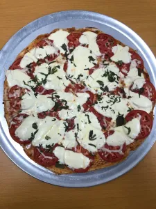Pizza with tomato slices, melted cheese, and fresh basil on a metal tray.